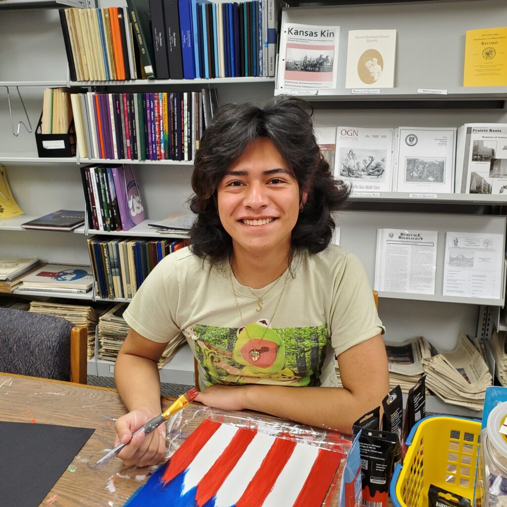 Summer Intern, Fabrizzio Kramer, practices a demonstration piece for the patriotic art project.