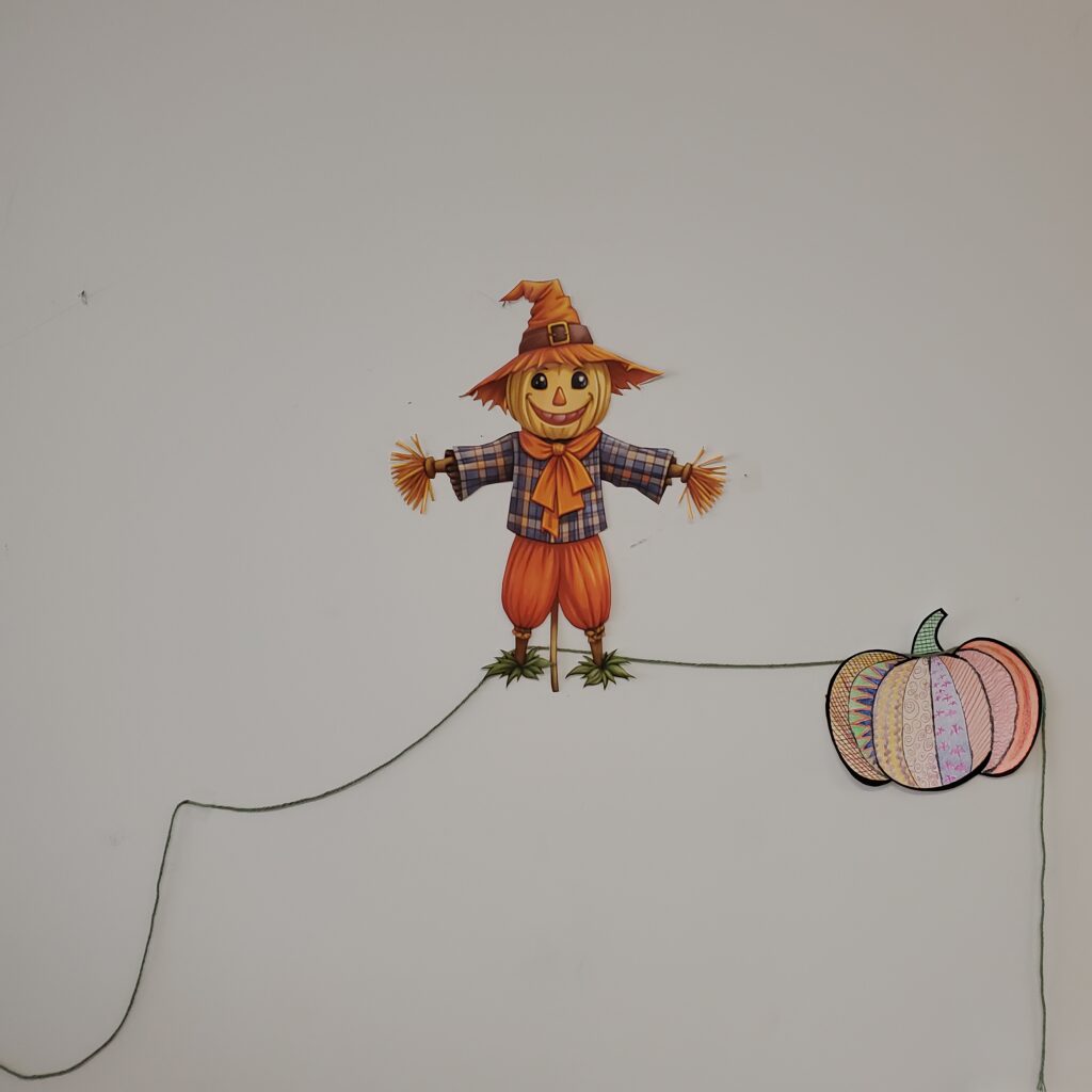 This Image depicts a scarecrow cutout and a decorated paper pumpkin demonstrating how the project will be displayed on the wall.