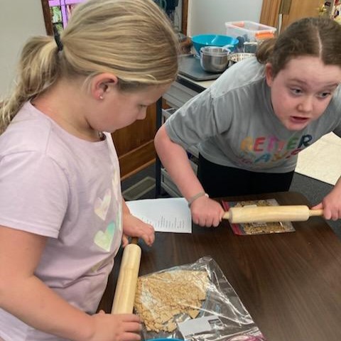 Participants crushing graham crackers in a bag using a rolling pin.