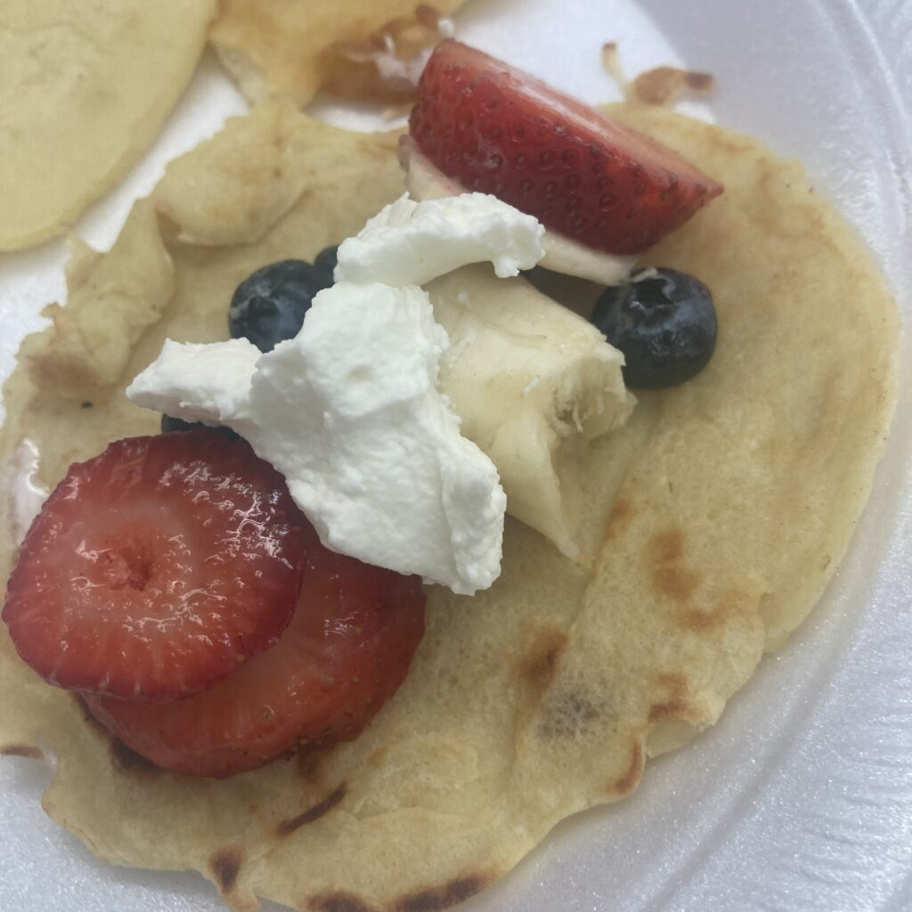 A crepe with whip creme, sliced strawberries, blue berries, and banana.