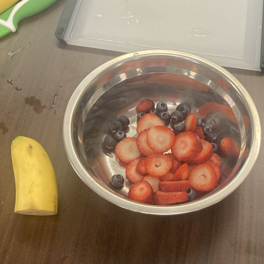 A half banana and a bowl of blue berries and sliced strawberries.