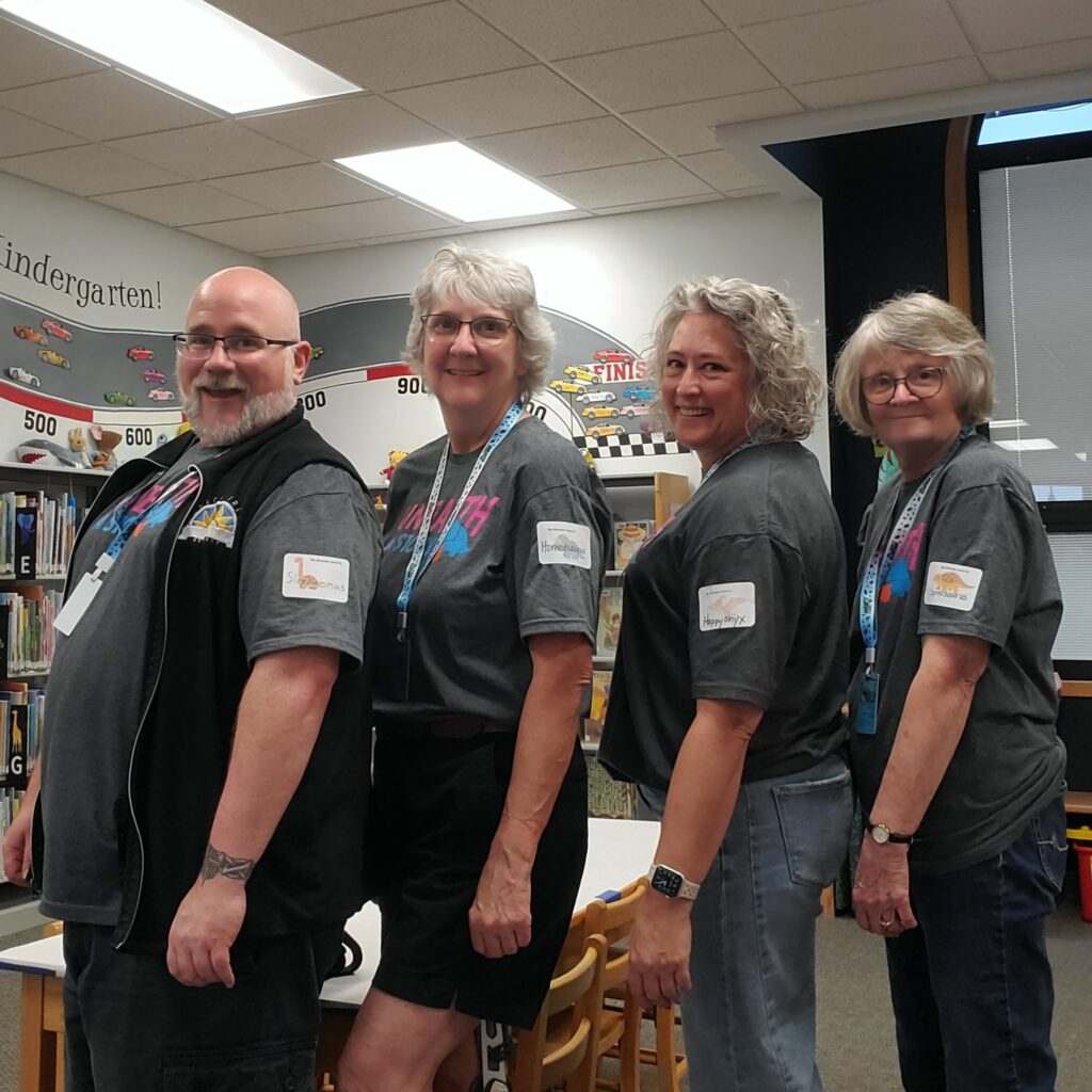 Chad Jones, Kate Haynie, Lori Bergman, Dee Lizzol showing Dinosaur Names name tags for the day. Staff also known as Sleepy-mimus, Horned-saurus, Happy-onyx, Spino-saurus.
